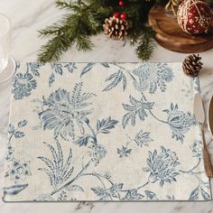 a place mat with blue flowers on it next to pine cones and other christmas decorations