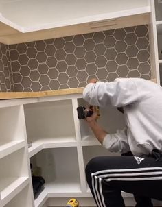 a man in white shirt and black pants working on shelves with wood trimmings