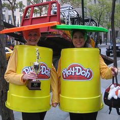 two people in costumes holding up large yellow buckets with the words play doh on them