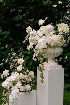 three white vases with flowers in them on the grass