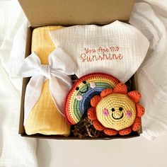 an open box containing a crocheted lion and a rainbow hat with a white ribbon