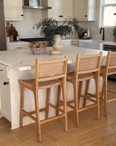 three wooden chairs sitting on top of a kitchen counter next to an island with white cabinets