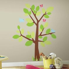 a child's room with a tree painted on the wall and stuffed animals nearby