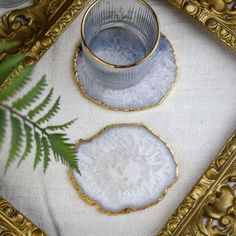 two pieces of glass with gold rims sitting on a white table cloth next to a fern leaf