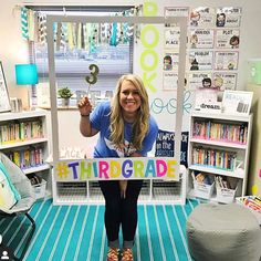 a woman holding up a sign that says thr grade in front of a room full of children's books