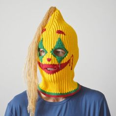 a person wearing a knitted clown mask with long blonde hair in front of a white background