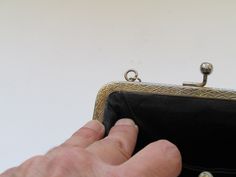 a hand is holding a black purse on a white surface with gold trimmings