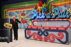 a man in a suit standing next to a video game machine with the words pick a pair on it