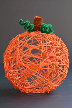 an orange string ball with a stuffed animal on top and green yarn in the middle