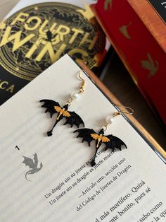 the earrings are black and gold with bats on them, sitting next to an open book