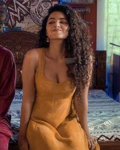 a woman sitting on top of a bed wearing a yellow dress and smiling at the camera