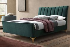 a bed with green velvet headboard and foot board in a bedroom area next to a window