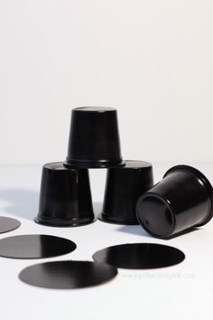 several black cups sitting next to each other on top of a white table with circles around them