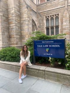 a woman sitting on the side of a building next to a blue sign that says vale law school