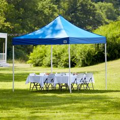 a blue and white tent is set up in the middle of a field with tables under it