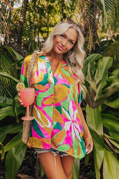 - Take a trip to paradise in this vibrant top! - Unlined material with a pink, yellow, and green hued abstract tropical print and a satin finish - A v-cut neckline with a pleated detail - Short draped sleeves - An oversized silhouette that ends in a straight hemline Colorful V-neck Blouse For Vacation, Tropical V-neck Top With Vibrant Print, Tropical V-neck Blouse For Beach, Colorful V-neck Blouse For Beach, Summer V-neck Blouse With Tropical Print, V-neck Tropical Print Blouse For Beach, Hawaiian V-neck Top With Tropical Print, Beachwear V-neck Tops With Tropical Print, V-neck Beach Top With Abstract Print