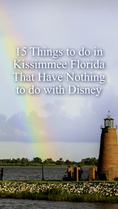 a rainbow in the sky over a body of water with a lighthouse and people standing near it