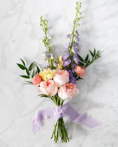 a bouquet of flowers on a white marble surface with purple ribbon and greenery around it