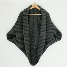 a gray sweater hanging on a wooden hanger with a white wall in the background