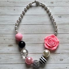 a necklace with pink roses, black and white beads and pearls on a wooden background