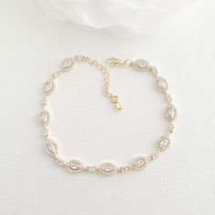 a white rose sitting on top of a table next to a gold bracelet with crystal stones