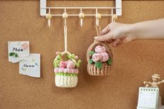 two small baskets with flowers hanging from hooks on a cork bulletin board next to a calendar