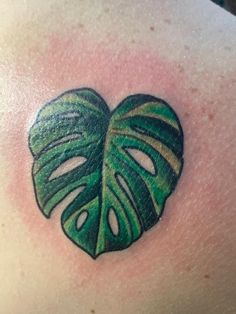 a green leaf tattoo on the back of a woman's shoulder