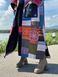 a woman in high heeled boots and a colorful patchwork coat is standing by the water