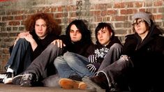 three young men sitting next to each other in front of a brick wall