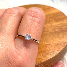 a woman's hand with a diamond ring on top of her finger next to a wooden object