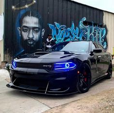 a blue car parked in front of a graffiti covered wall with a man's face on it