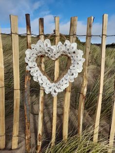 a heart - shaped glass wreath hangs on a fence in front of sand dunes and grass