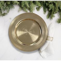 a gold plate sitting on top of a white counter next to pine branches and napkins