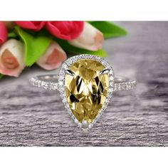 a yellow diamond ring sitting on top of a wooden table next to flowers and tulips