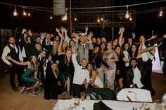 a large group of people posing for a photo at a party with their hands in the air