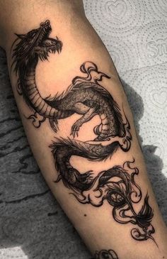 a black and white photo of a dragon tattoo on the leg