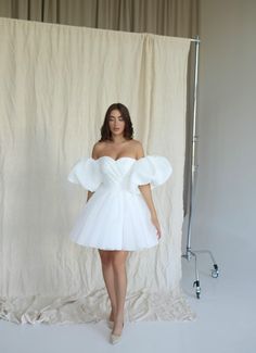 a woman standing in front of a white backdrop wearing a dress with puffy sleeves