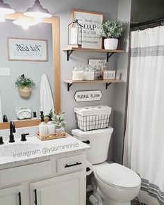 a white toilet sitting under a bathroom mirror next to a sink and a shower curtain