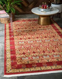 a red rug with an intricate design on the floor next to a coffee table and potted plant