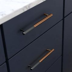 the handles on two drawers are gold and black, with marble countertop in the background