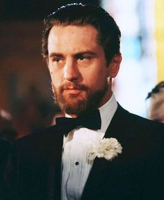 a man in a tuxedo and bow tie looks off to the side as he stands