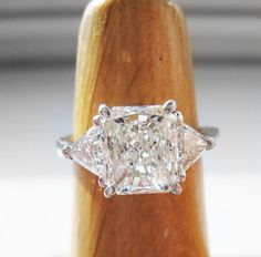 an engagement ring with three princess cut diamonds set in the shans on a wooden stand