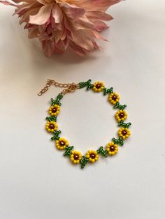 a yellow and green bracelet with flowers on it next to a pink flower bouquet in the background