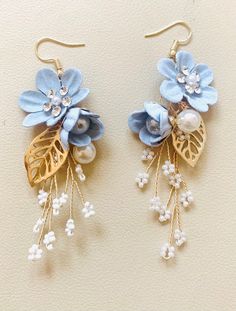 two pairs of earrings with blue flowers and pearls hanging from the ear hooks on a white surface