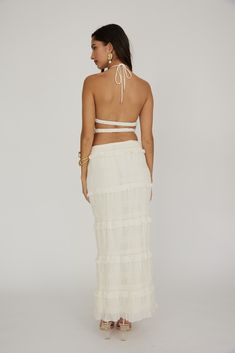 the back of a woman wearing a white dress with ruffled skirt and halter top