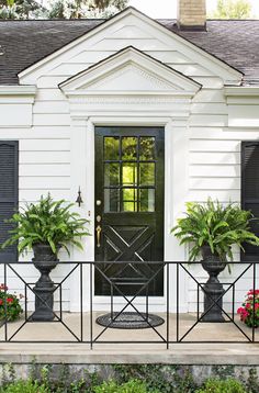 the front door of a white house with black shutters and potted plants on either side