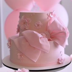 a three tiered cake with pink flowers and bows on it's side, surrounded by balloons