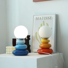 a colorful lamp sitting on top of a white table next to a framed photograph and bead balls