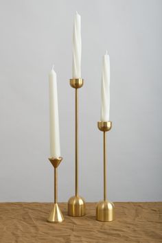 three brass candlesticks on a wooden table with one white candle in the middle