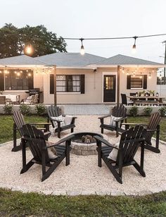 a fire pit surrounded by lawn chairs and string lights in front of a white house